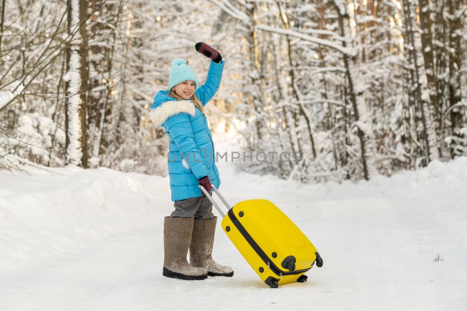 A girl in winter in felt boots goes with a suitcase on a frosty snowy day by Lobachad