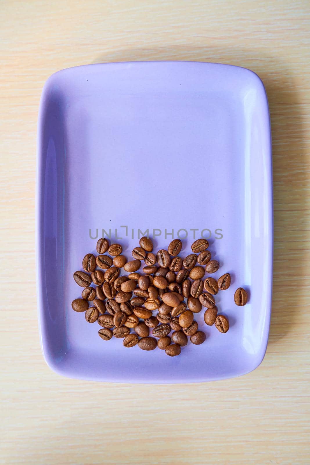 A heap of coffee beans lies on a purple plate. Top view. Copy space
