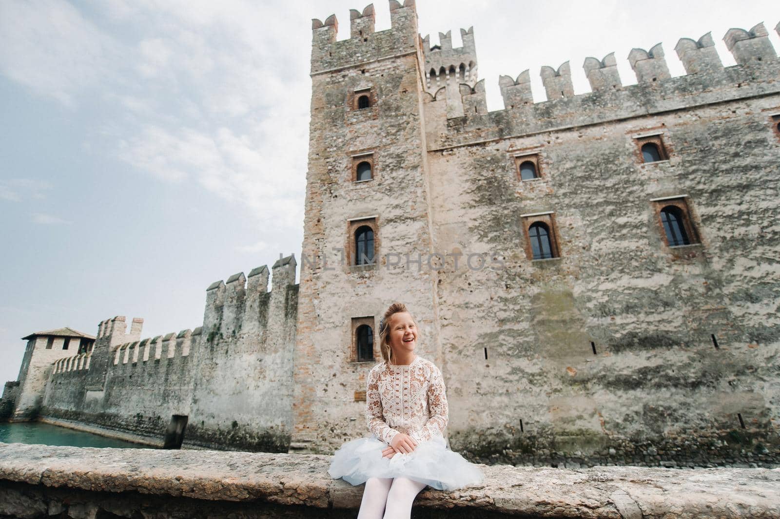 a little girl in a white dress on the background of the old castle in the city of Sirmione.Italy.