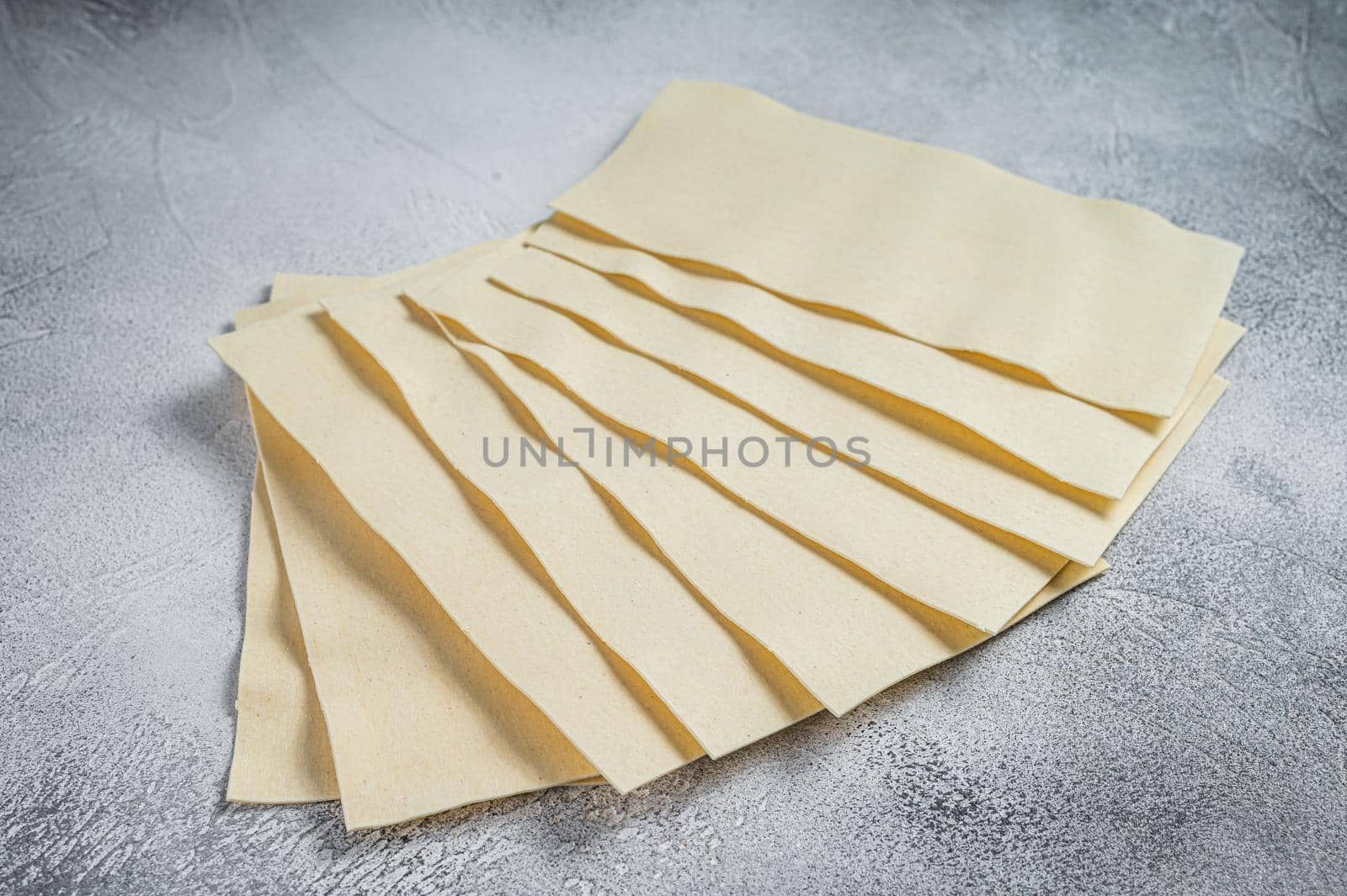 Raw lasagna sheets stack on a kitchen table. White background. Top view by Composter
