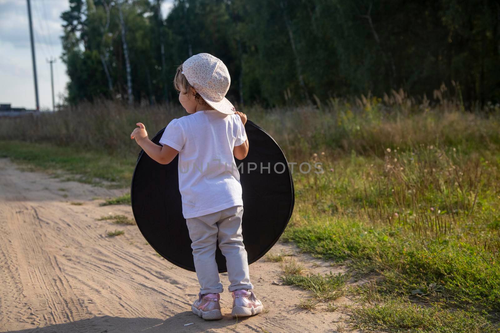 a toddler holds a reflector for the photographer on the country road. little helper assistant
