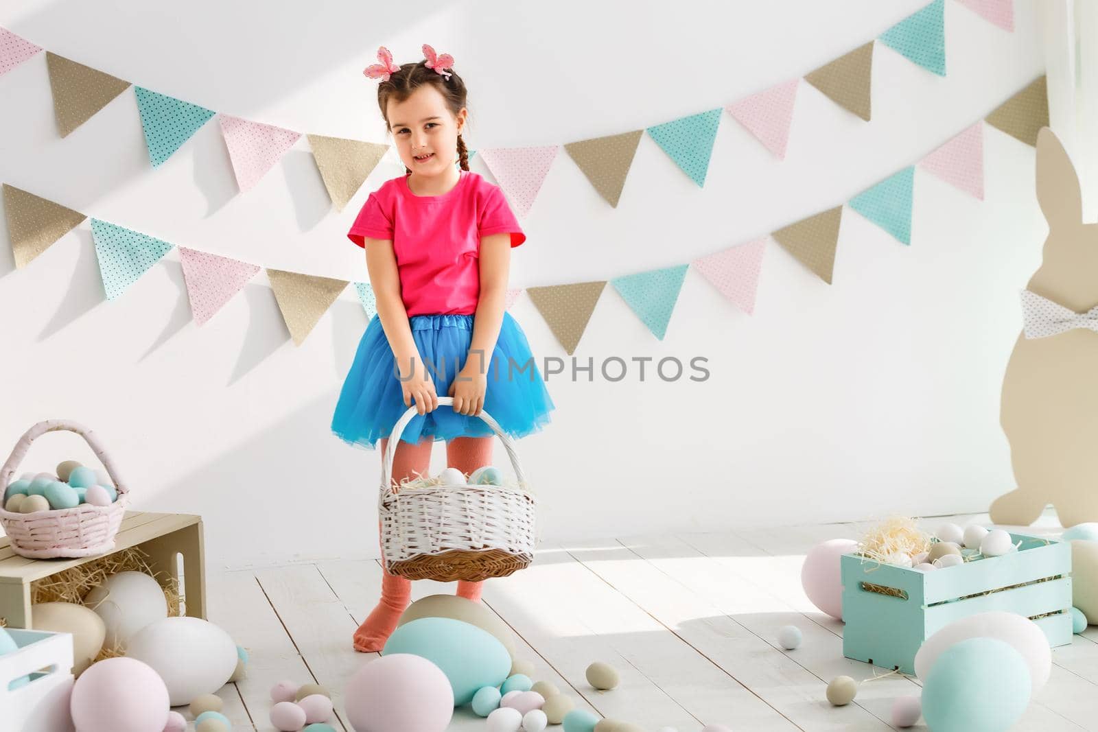 Getting ready to Easter. Lovely little girl holding an Easter egg and smiling with decoration in the background