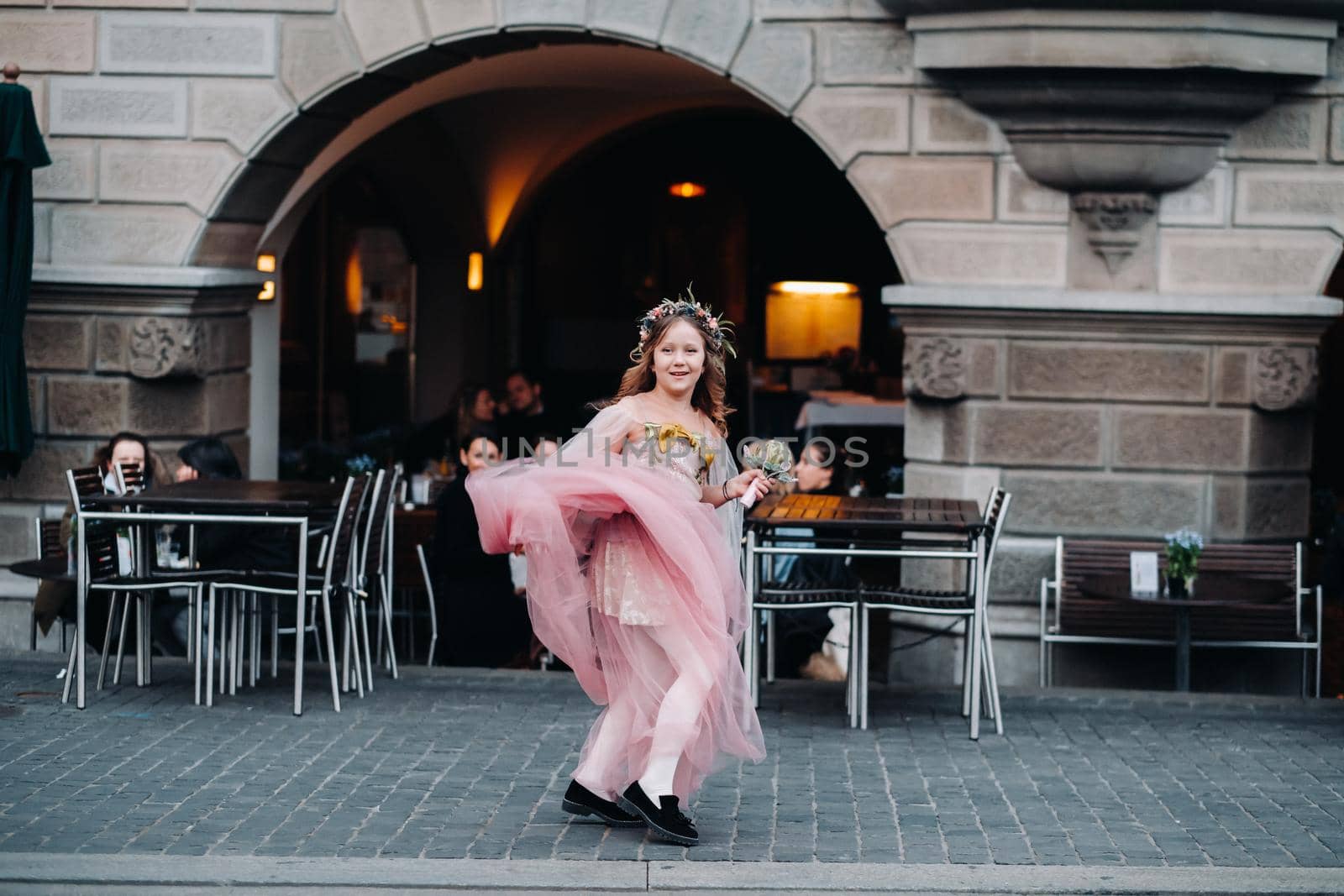 a little girl in a pink Princess dress with a bouquet in her hands walks through the old city of Zurich.Portrait of a girl in a pink dress on a city street in Switzerland.