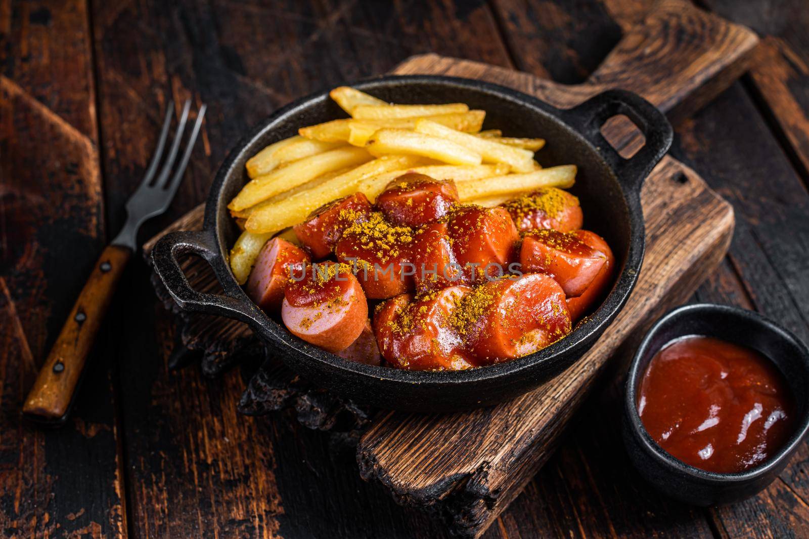 Currywurst street food meal, Curry spice on wursts served French fries in a pan. Dark wooden background. Top view.