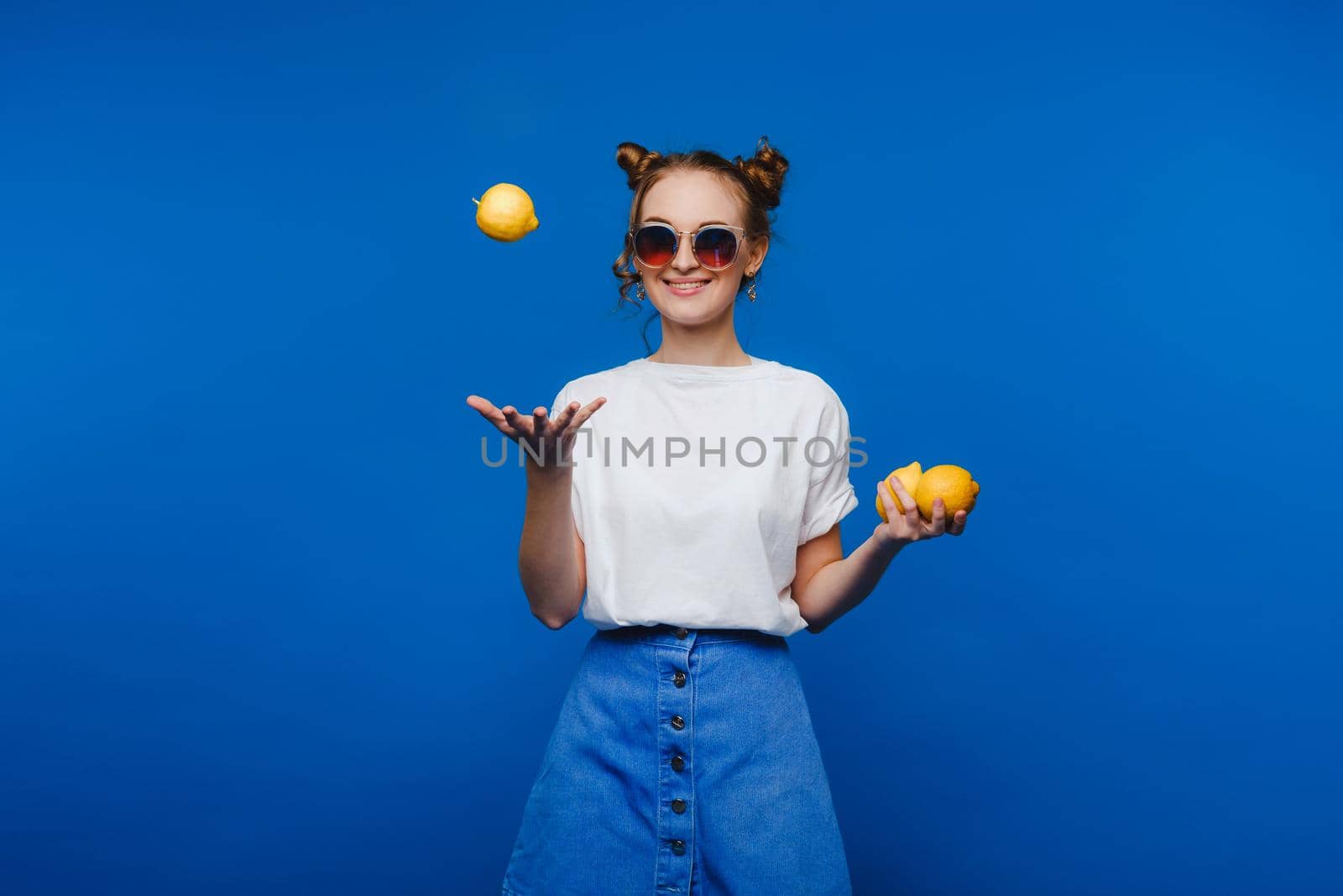 Young beautiful smiling women with curly hair tasting sour lemon halves emotionally. Funny girl with wavy hairstyle and bright make up isolated over yellow background. Copy space. Yellow lifestyle