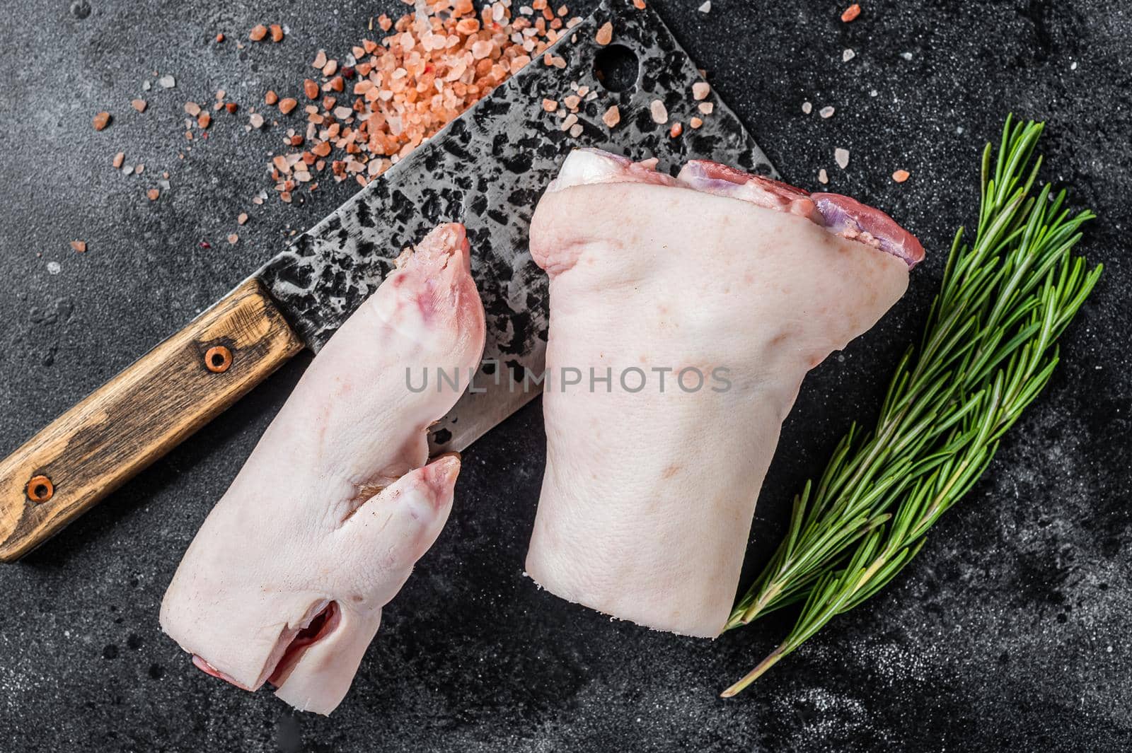 Butcher shop - Raw pork hoof, knuckle, feet on a cutting board. Black background. Top view.
