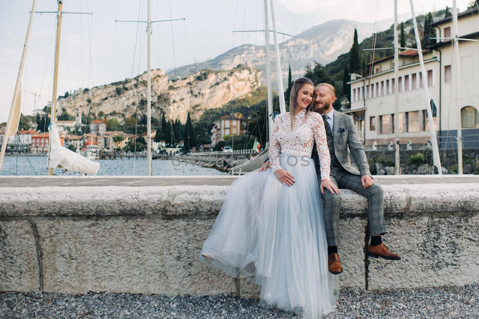 Italy, Lake Garda. A beautiful couple on the shores of lake Garda in Italy at the foot of the Alps.A man and a woman sit on a pier in Italy by Lobachad