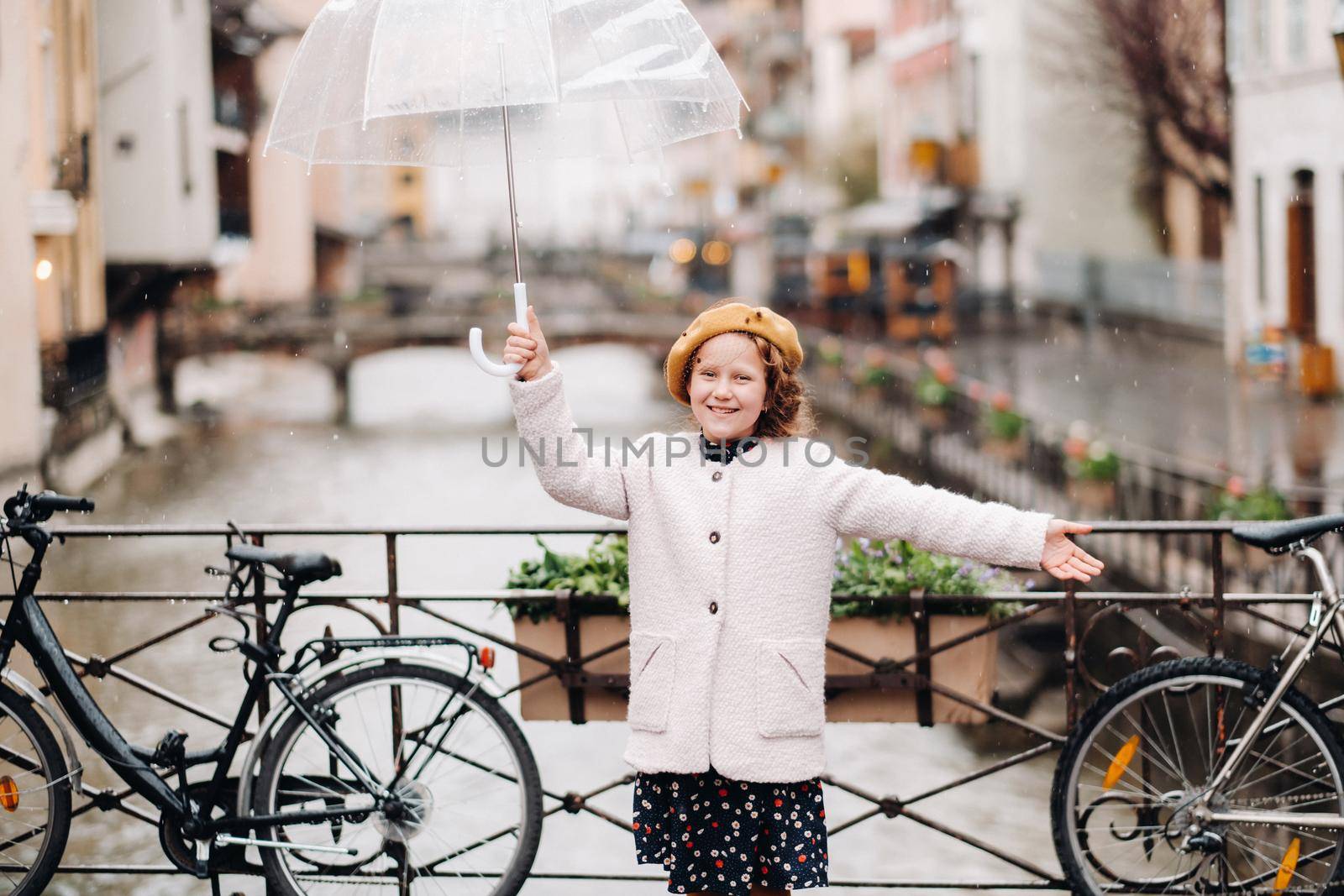 cheerful beautiful girl in a coat with a transparent umbrella in Annecy. France. The girl Cheerfully raises an umbrella in the rain. by Lobachad