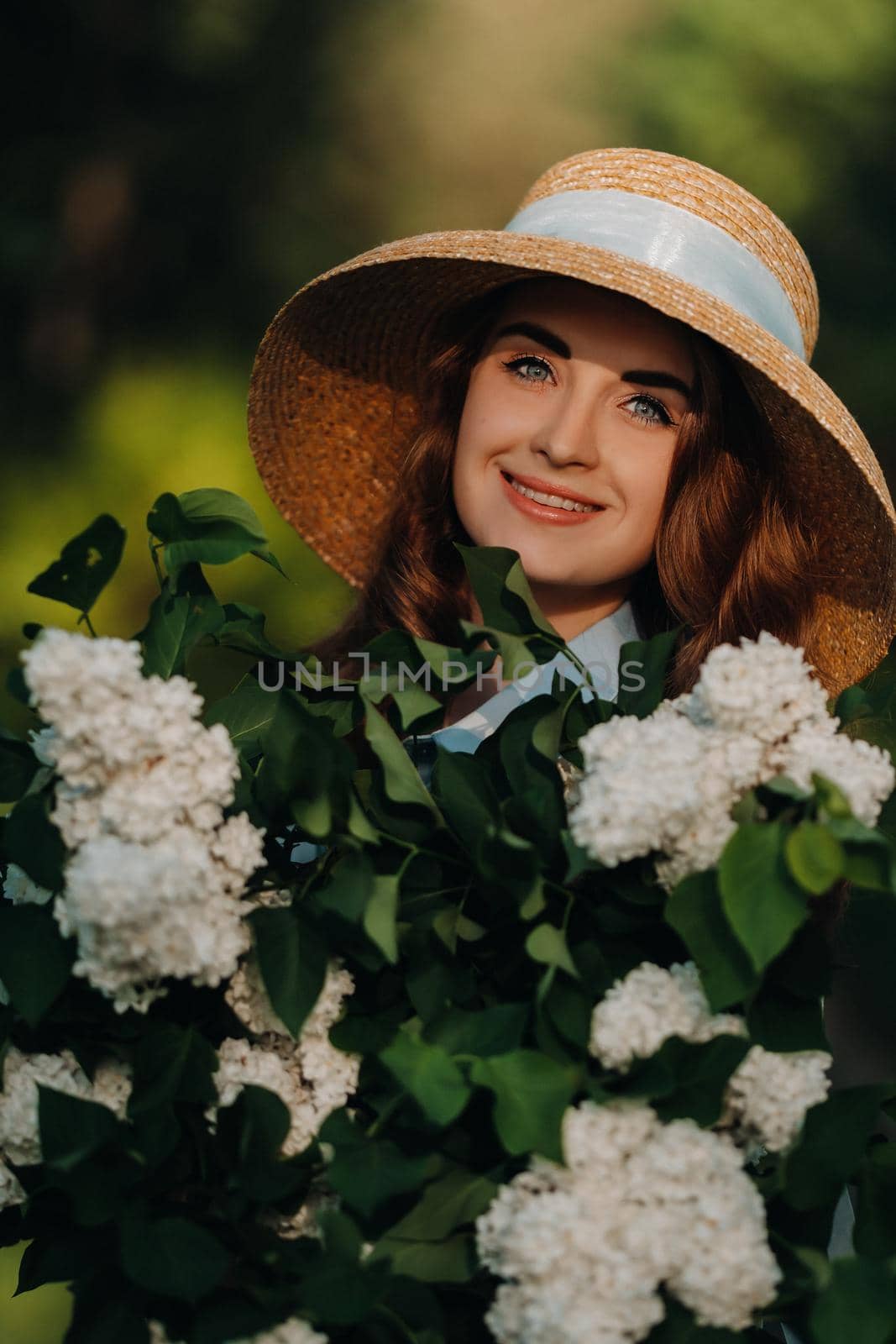 Portrait of a beautiful girl with long hair, a straw hat and a long summer dress with lilac flowers in the garden.
