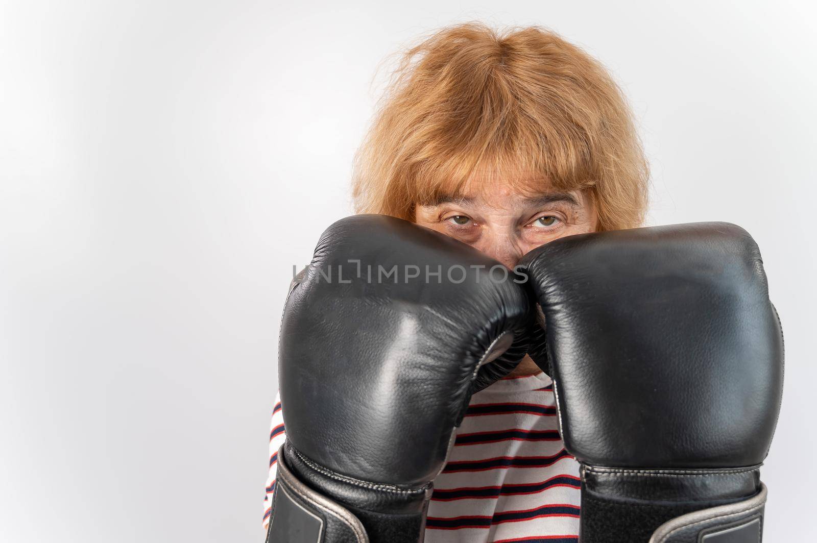 Elderly woman in fighting gloves in a defensive pose on a white background