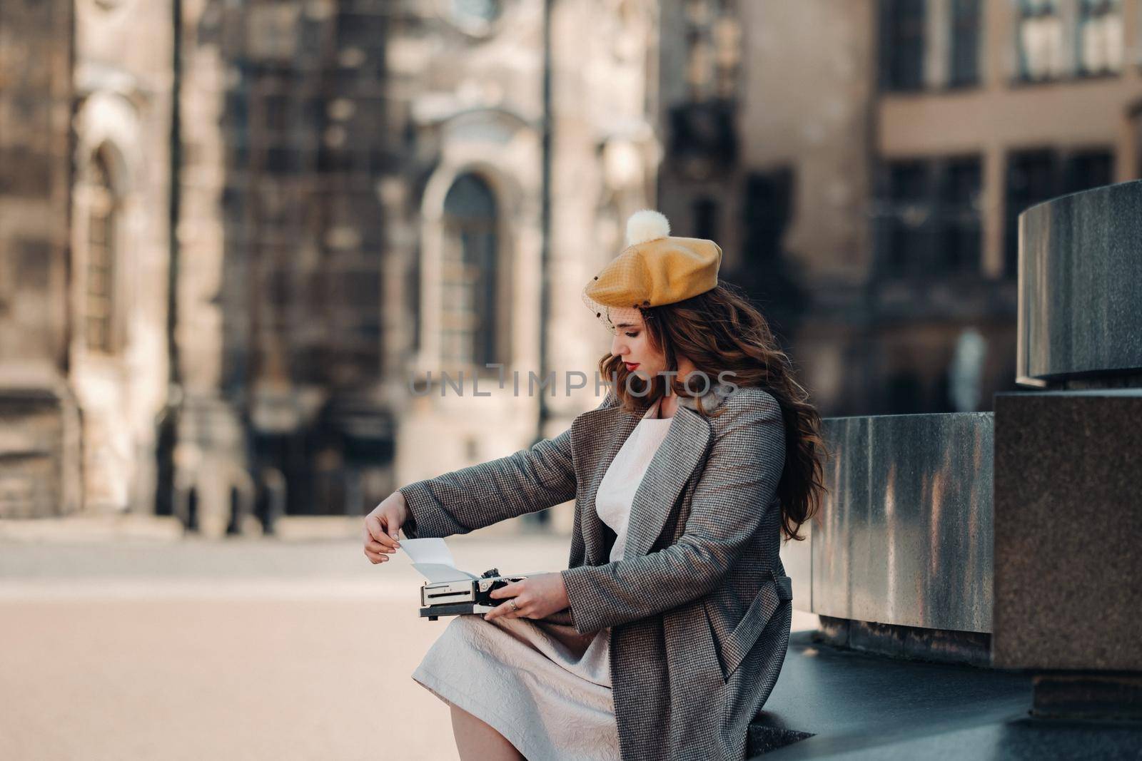 a stylish young beautiful girl is sitting and typing in the Old town of Dresden.Germany. by Lobachad