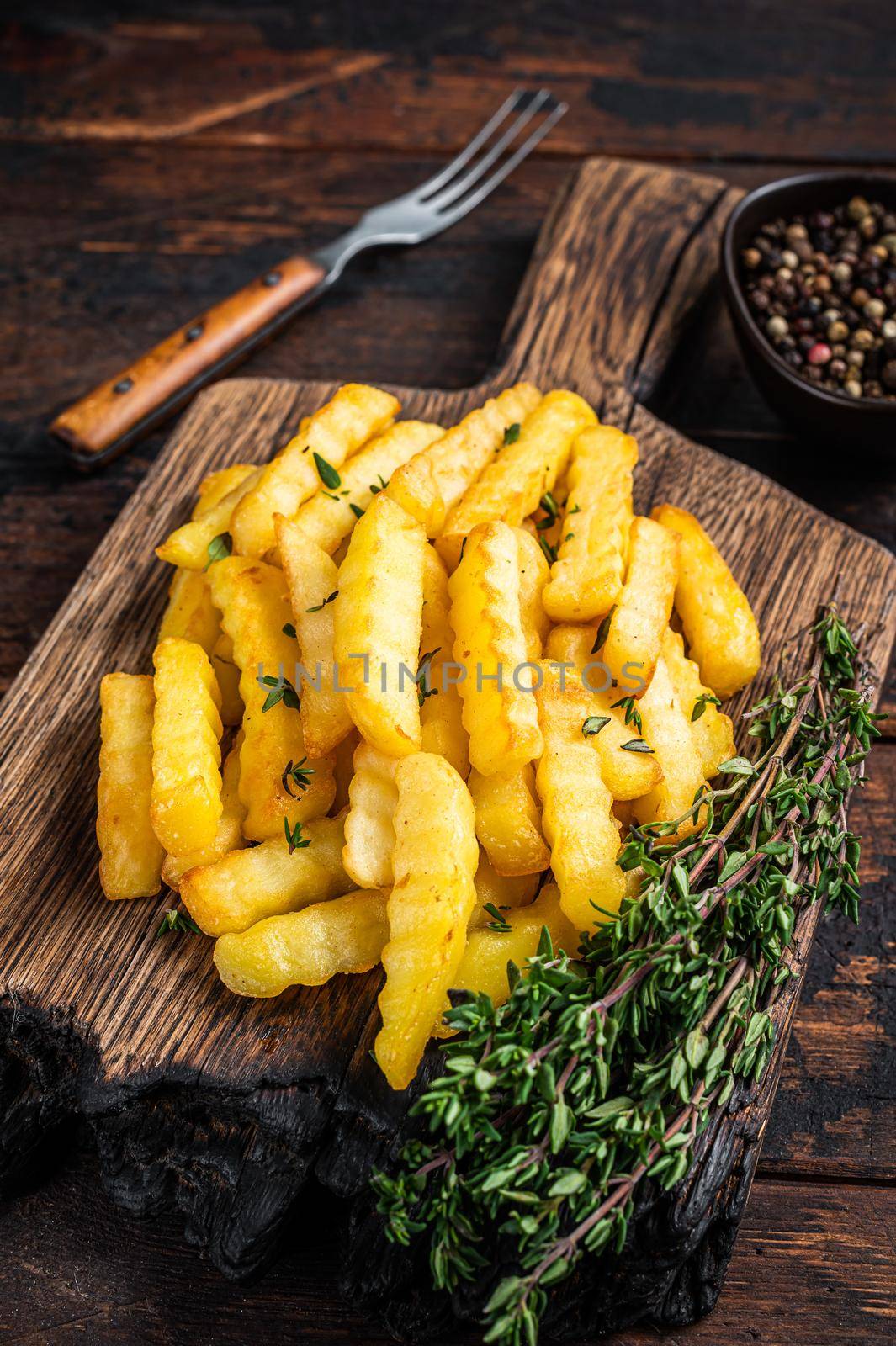Baked Crinkle French fries potatoes sticks or chips on a wooden board. Dark wooden background. Top view by Composter
