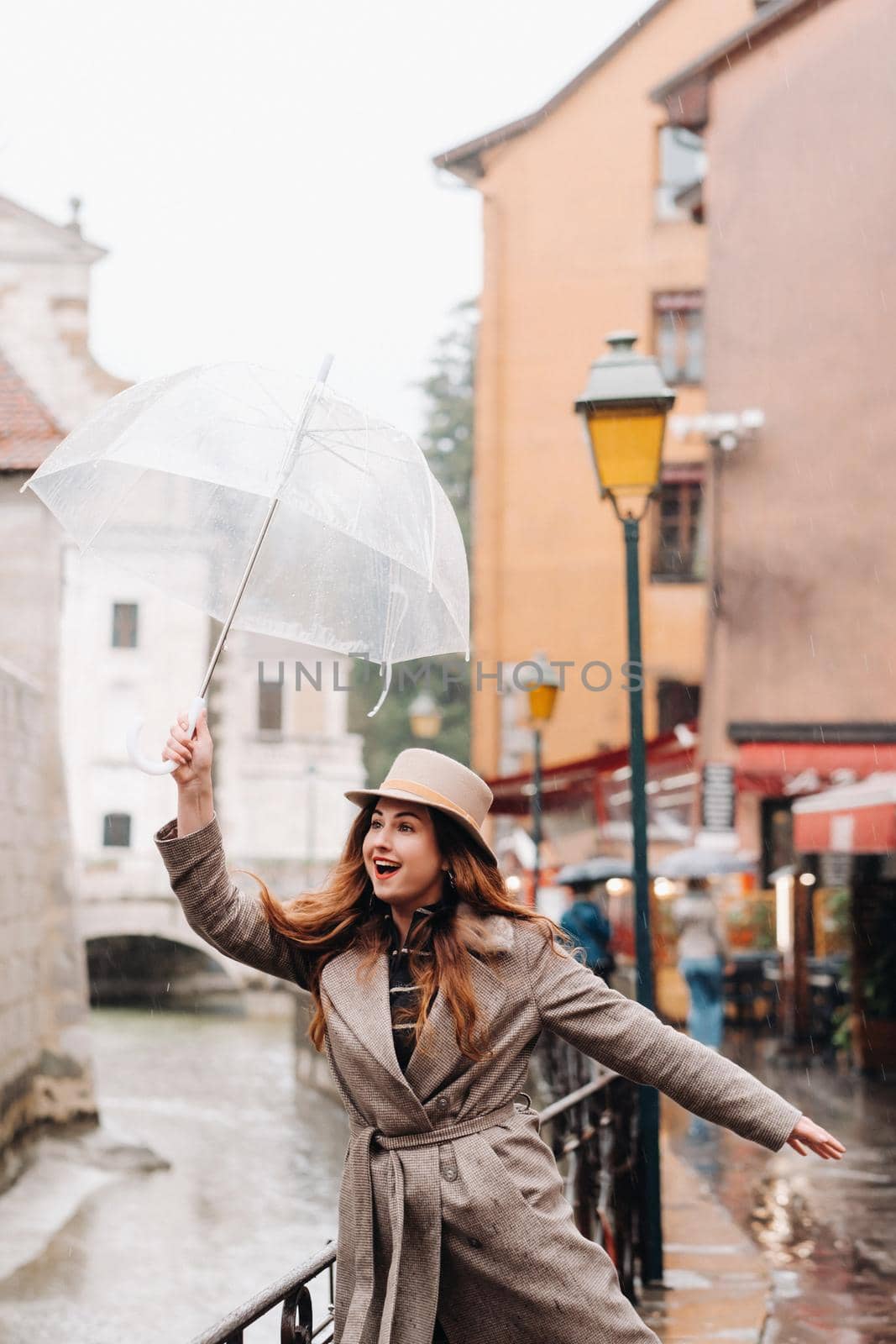 beautiful romantic girl in a coat and hat with a transparent umbrella in Annecy. France. The girl in the hat in France by Lobachad