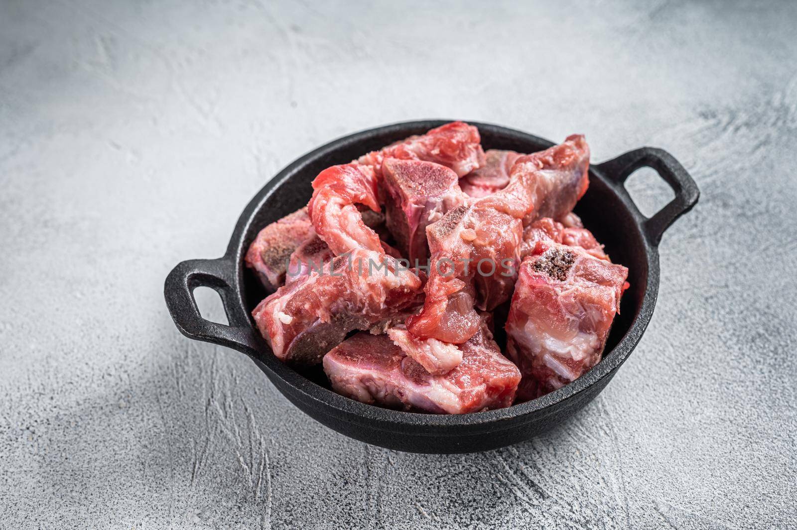 Raw diced meat cubes with bone in a pan. White background. Top View.