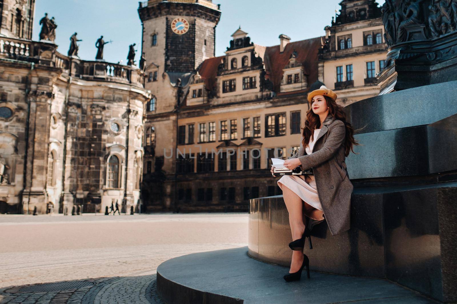 a stylish young beautiful girl is sitting and typing in the Old town of Dresden.Germany. by Lobachad