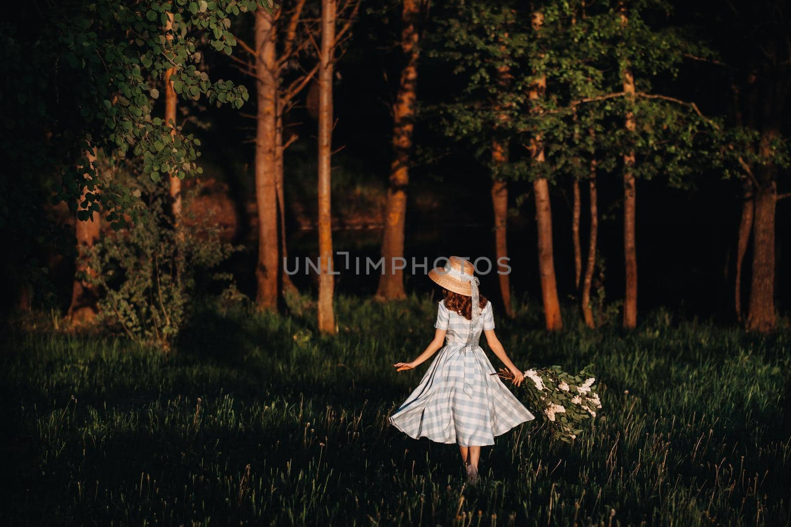 Beautiful girl enjoying the smell of lilac on a summer day. Aromatherapy and spring concept. A pretty girl, a beautiful woman in a blue long vintage dress is standing in a lilac garden. Gardening.