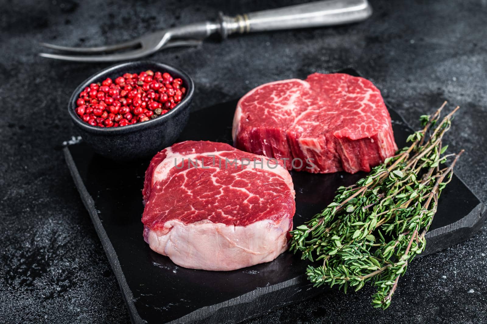 Prime Raw Fillet Mignon tenderloin steaks with thyme. Black background. Top view.