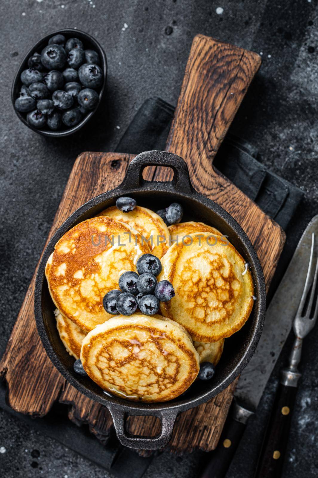 Pancakes with fresh blueberries and maple syrup in a pan. Black background. Top View by Composter