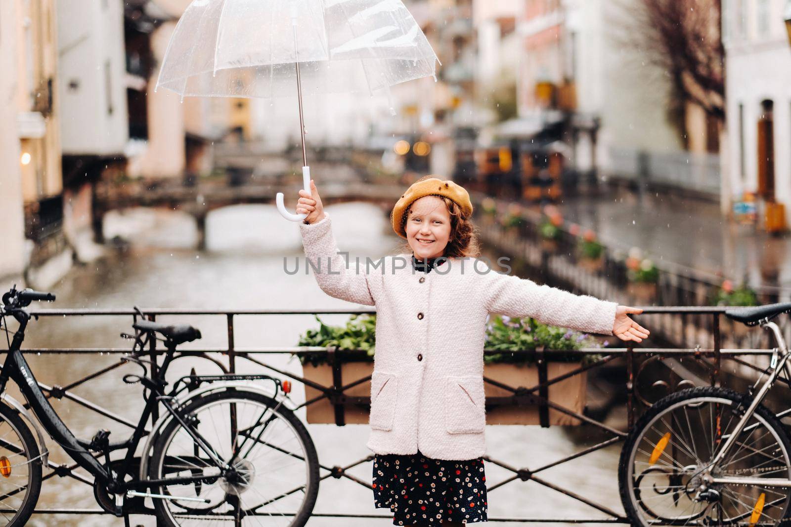 cheerful beautiful girl in a coat with a transparent umbrella in Annecy. France. The girl Cheerfully raises an umbrella in the rain