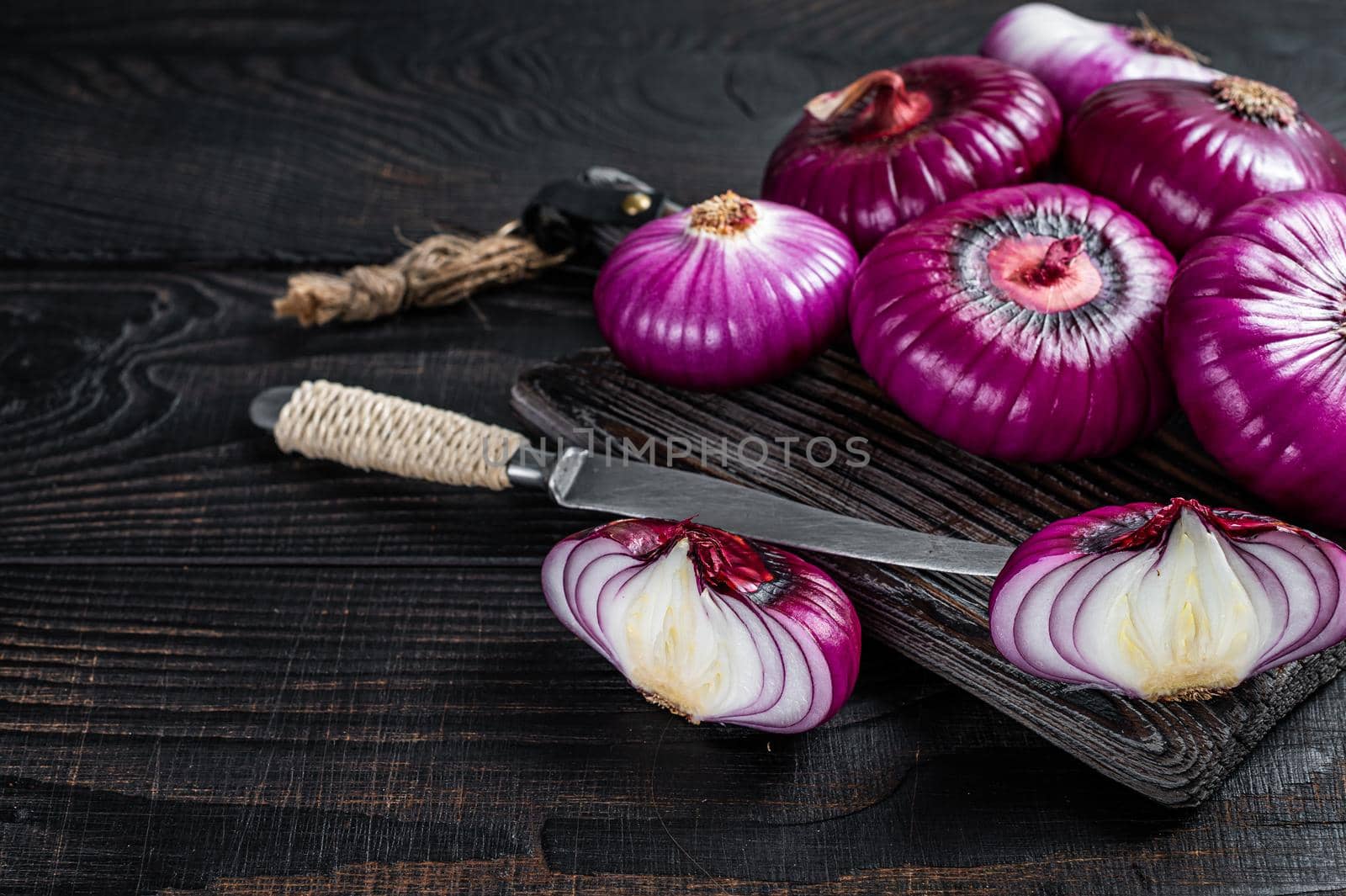 Whole and halfed Flat red sweet onion on a cutting board. Black Wooden background. Top View. Copy space by Composter