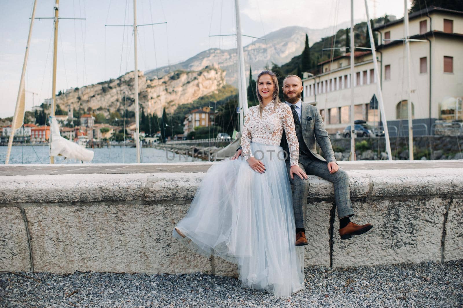 Italy, Lake Garda. A beautiful couple on the shores of lake Garda in Italy at the foot of the Alps.A man and a woman sit on a pier in Italy by Lobachad