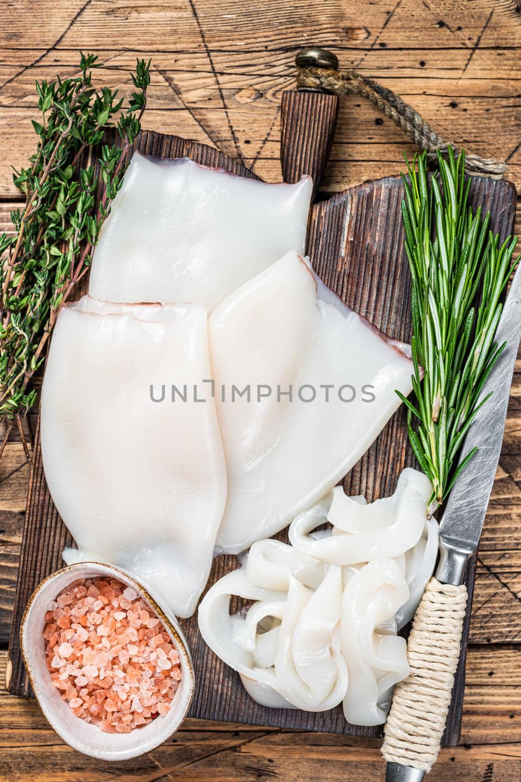 Sliced rings Raw Calamari or Squid on a wooden board with rosemary. wooden background. Top view.