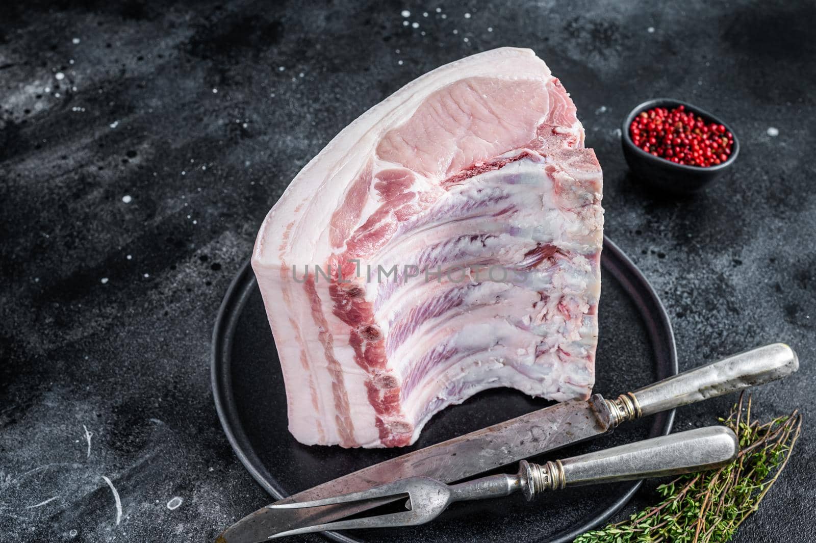Fresh Raw whole rack of pork loin chops with ribs on a plate with meat fork. Black background. Top view by Composter