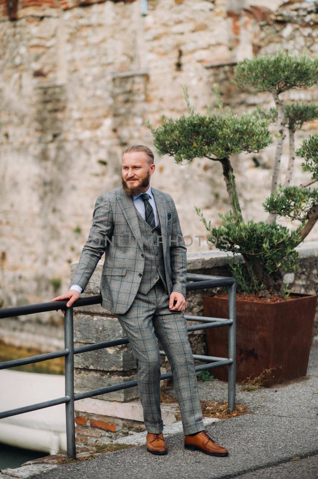 A man with a beard in a strict grey three-piece suit with a tie in the old town of Sirmione, a Stylish man in a grey suit in Italy.