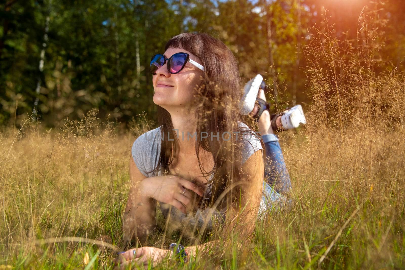 beautiful young woman in sunglasses enjoys the sun on the grass by Mariaprovector
