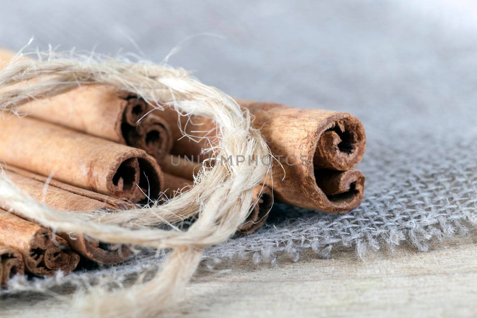 whole solid cinnamon sticks tied with a rope and lying on linen material and an old wooden surface, close-up on the side