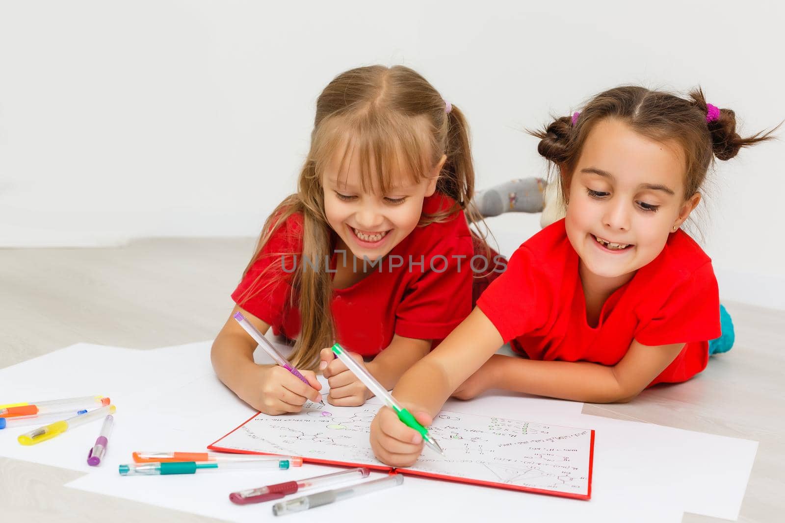 family, leisure and childhood concept - happy sisters lying on floor and drawing and doing homework at home