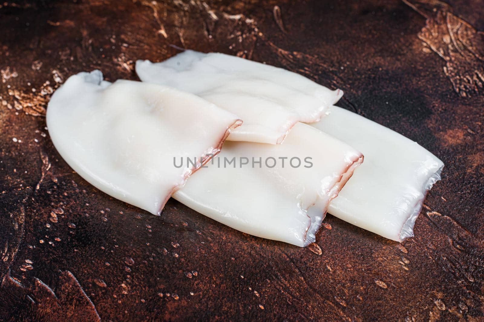 Raw Squid or Calamari tubes on a kitchen table. Dark background. Top view by Composter