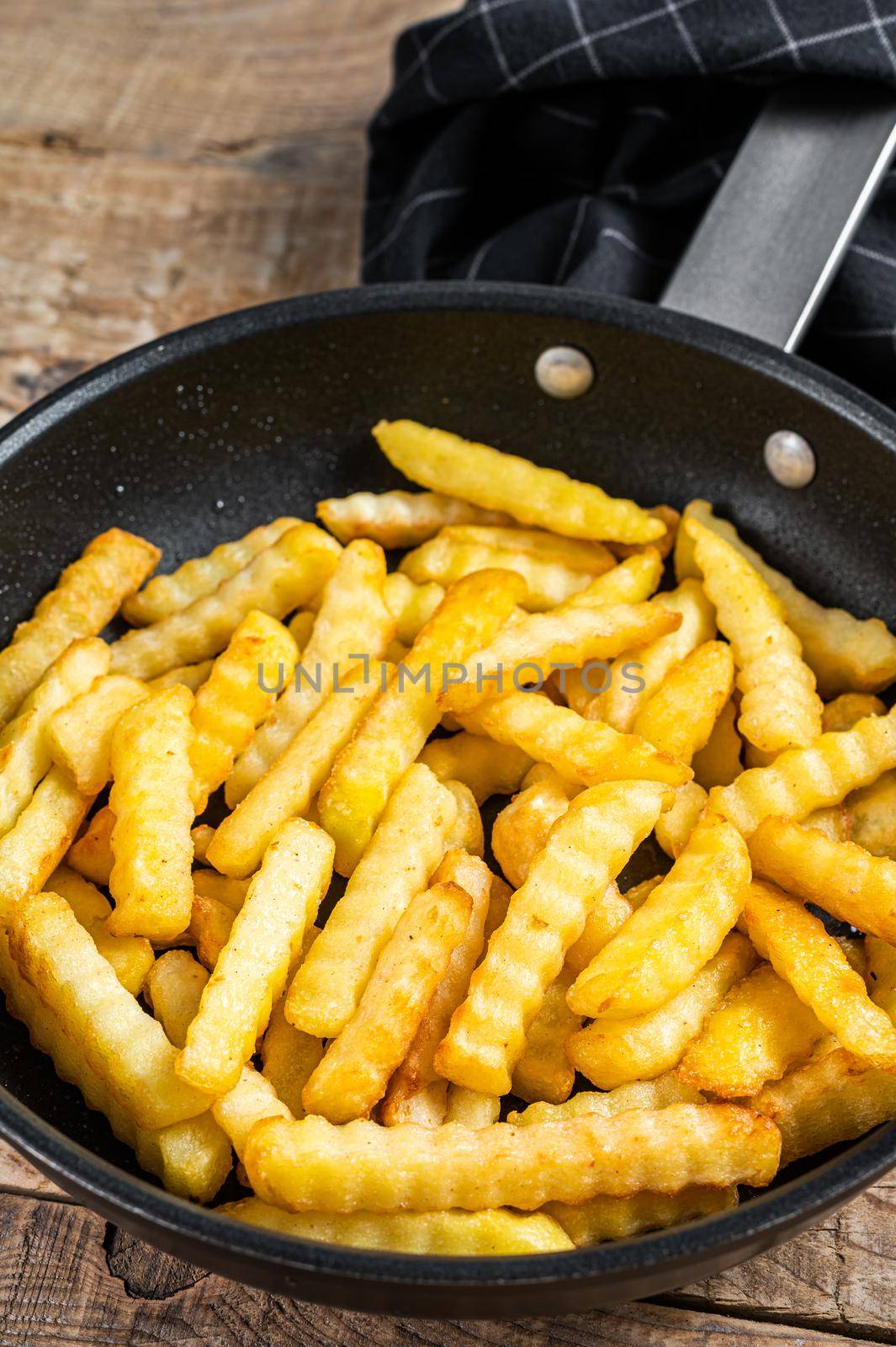 Deep fried Crinkle French fries potatoes sticks in a pan. Wooden background. Top view by Composter