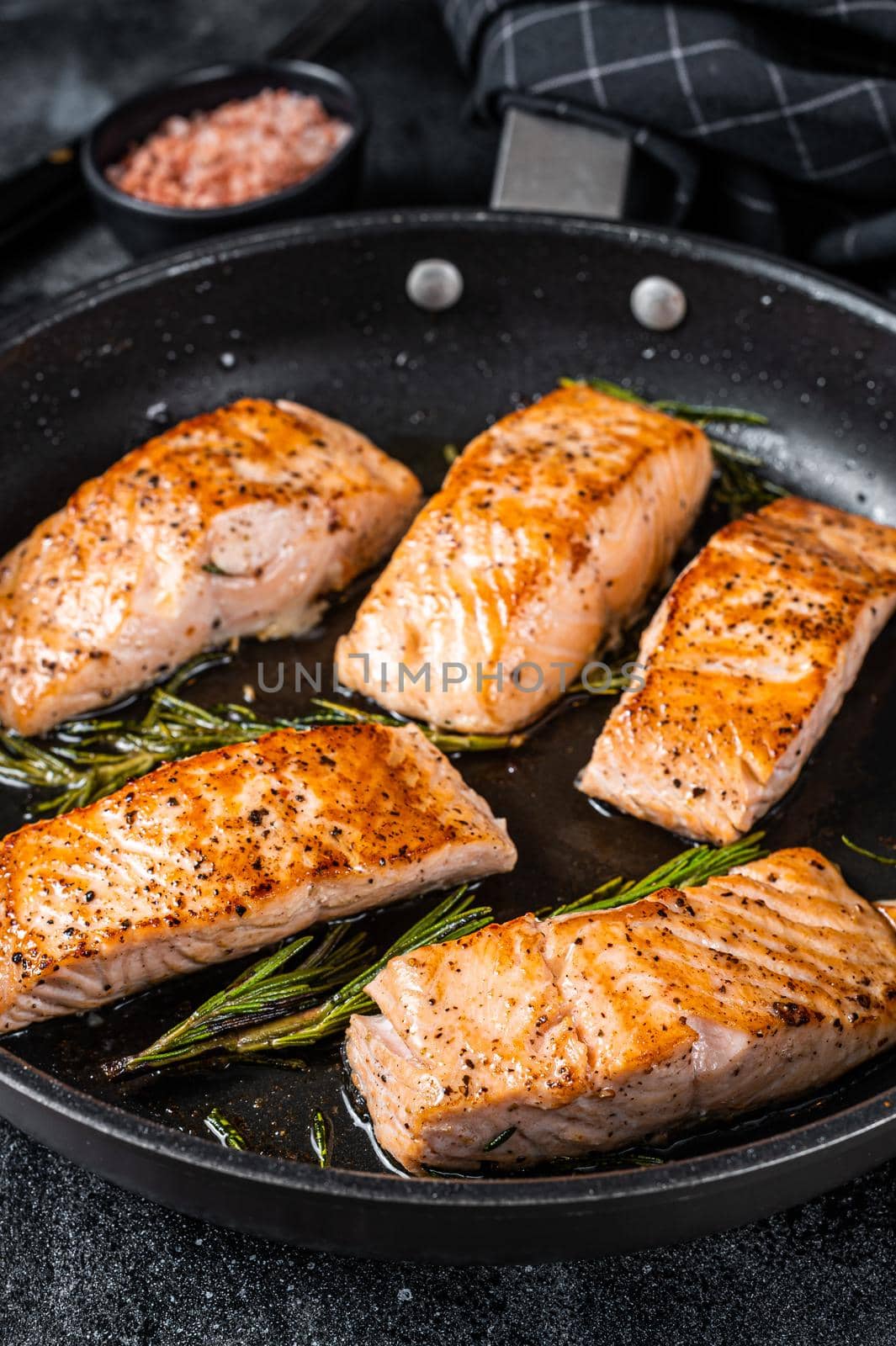 Roasted Salmon Fillet Steak in a pan with rosemary. Black background. Top view by Composter