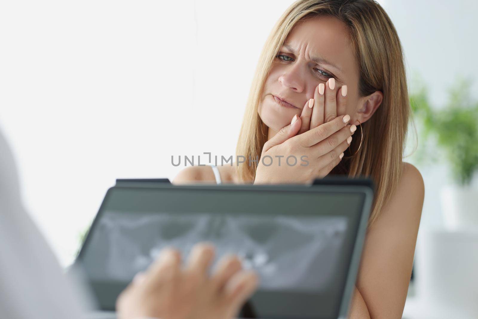 Portrait of woman on dentist appointment in clinic, patient suffer with strong tooth pain. Doctor investigate tooth scan on tablet, x ray result. Healthcare, stomatology concept