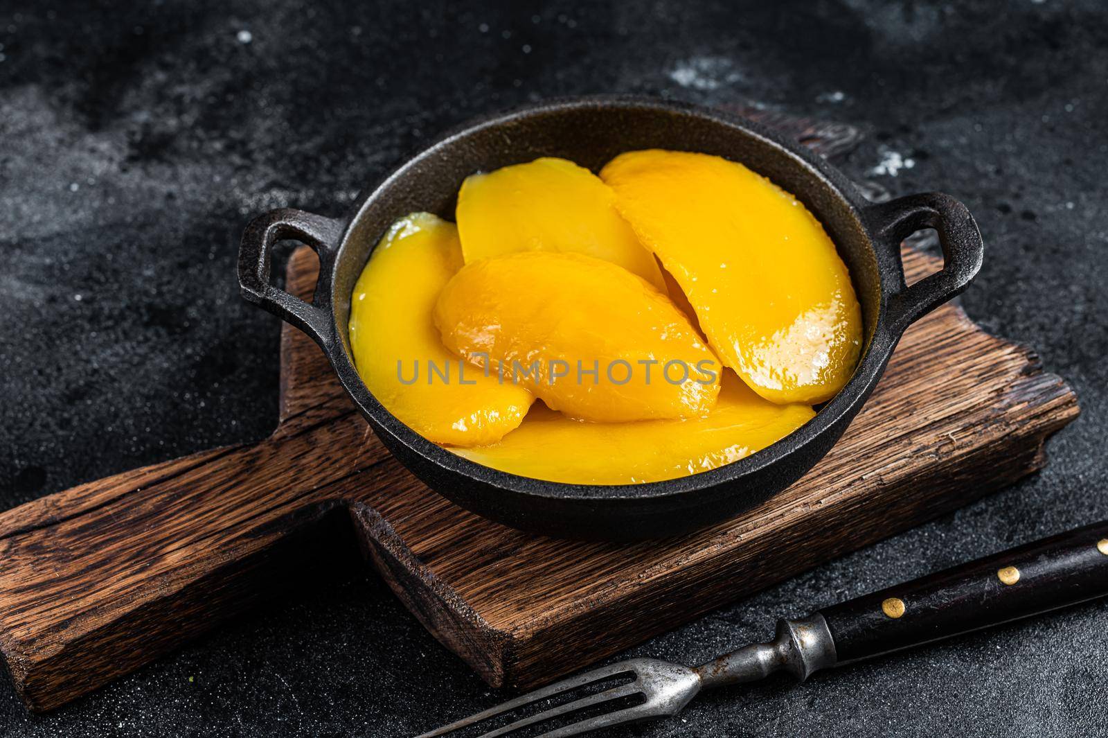 Canned mango slices in bowl. Black background. Top view by Composter