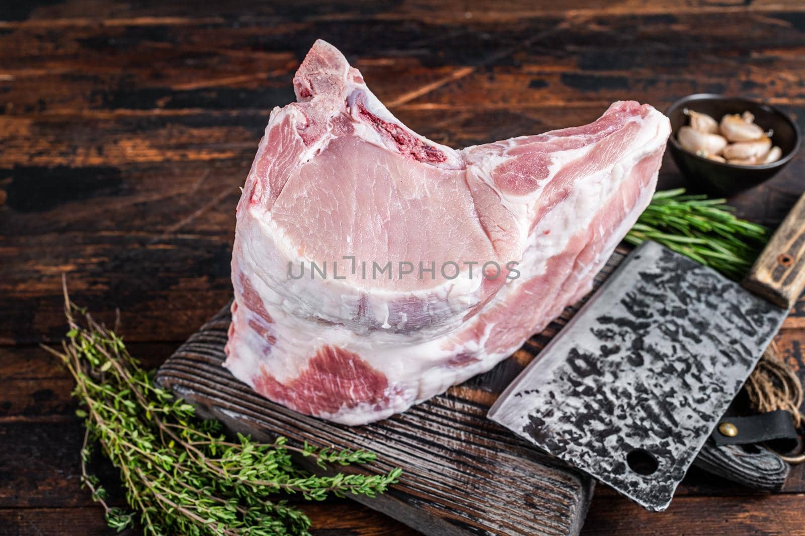 Raw rack of pork loin chops with ribs on a butcher board with meat cleaver. Dark wooden background. Top view by Composter