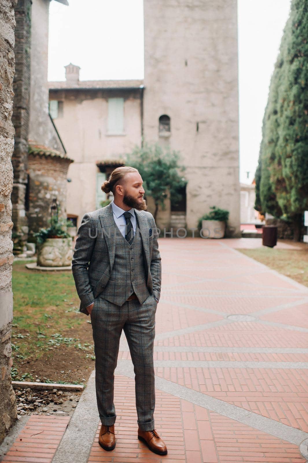 A man with a beard in a strict grey three-piece suit with a tie in the old town of Sirmione, a Stylish man in a grey suit in Italy.