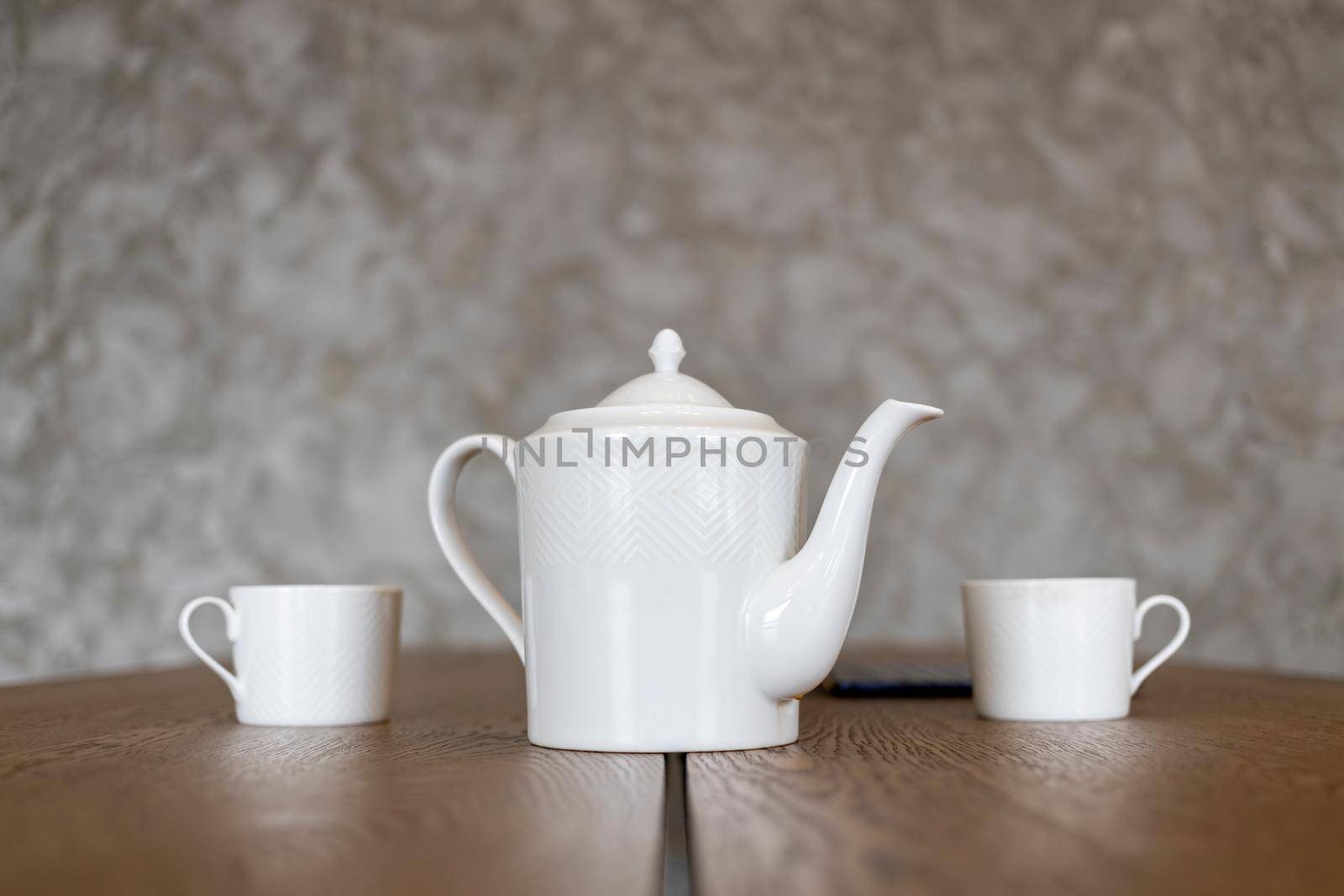 white tea set teapot and two cups stand on a brown table close up, no people