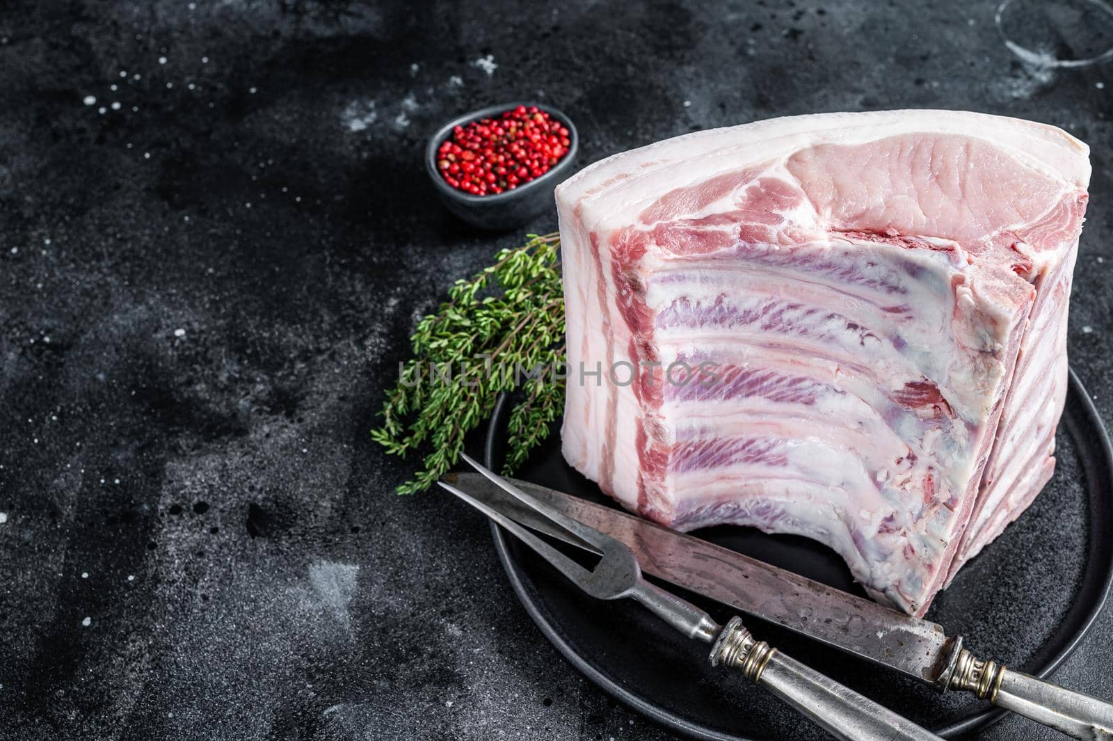 Fresh Raw whole rack of pork loin chops with ribs on a plate with meat fork. Black background. Top view. Copy space.