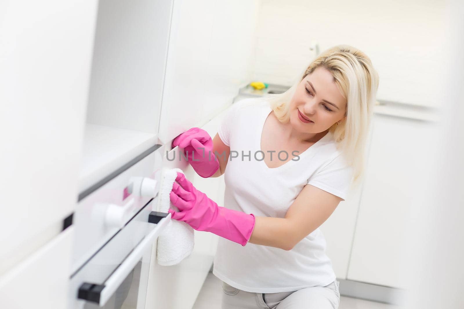 Woman in the kitchen is smiling and wiping dust using a spray and a duster while cleaning her house, close-up by Andelov13
