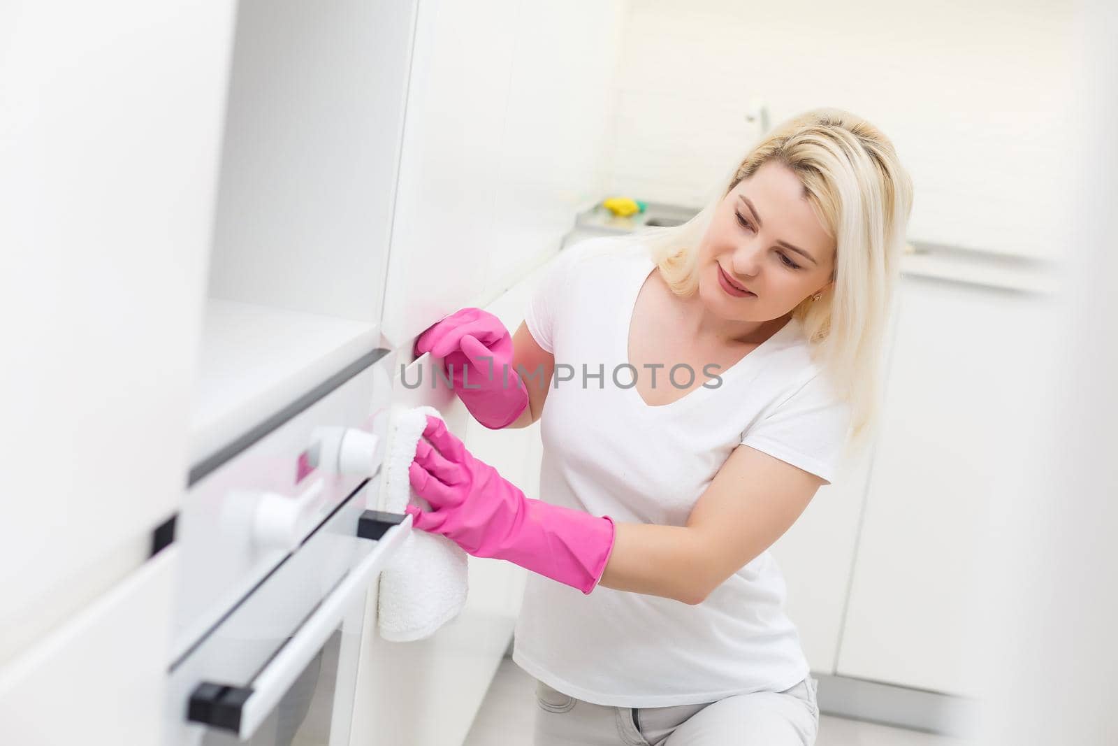 Woman in the kitchen is smiling and wiping dust using a spray and a duster while cleaning her house, close-up