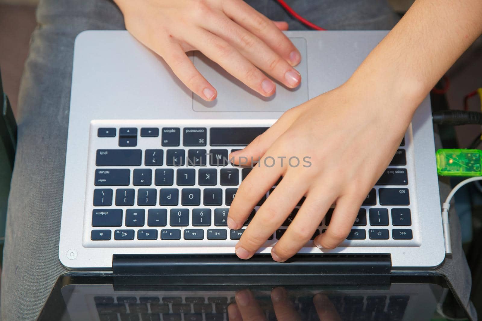 The boy is working on a computer on his lap . A cute Caucasian boy sitting on the bench in the park with his laptop on his knees and laughing