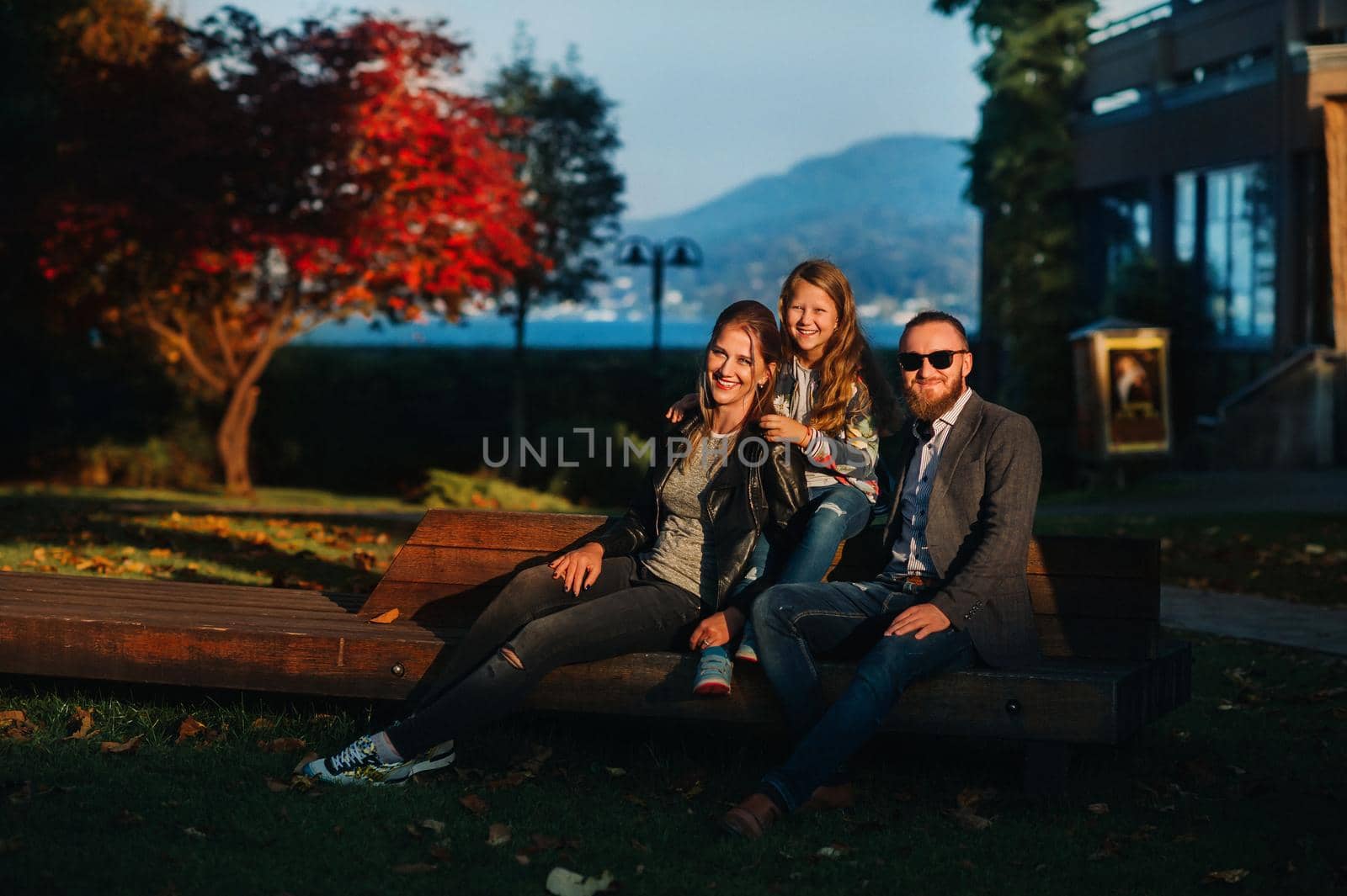 A happy family of three sits on a bench at a Sunny autumn sunset in Austria's Old town.A family poses in a small Austrian town against the backdrop of the Austrian Alps.Europe.Felden am see.