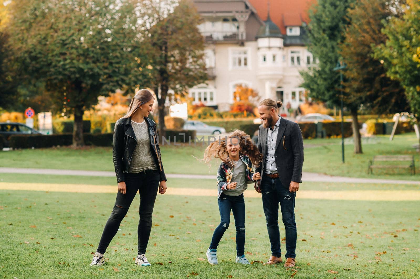 A happy family of three runs through the grass in Austria's old town.A family walks through a small town in Austria.Europe.Velden am werten Zee.