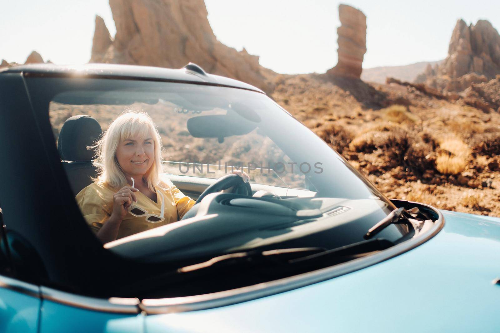 Girl in yellow dress enjoying a road trip in a convertible through a deserted valley with mountains, Canary Islands, Tenerife