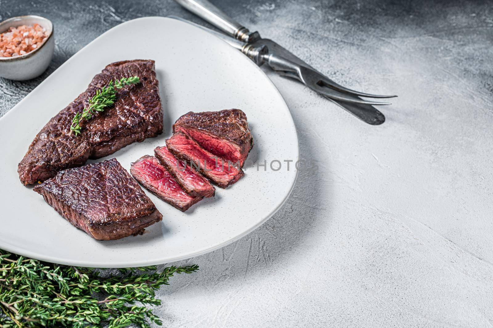 Roasted sliced rump beef meat steak on a plate with thyme. White background. Top view. Copy space by Composter