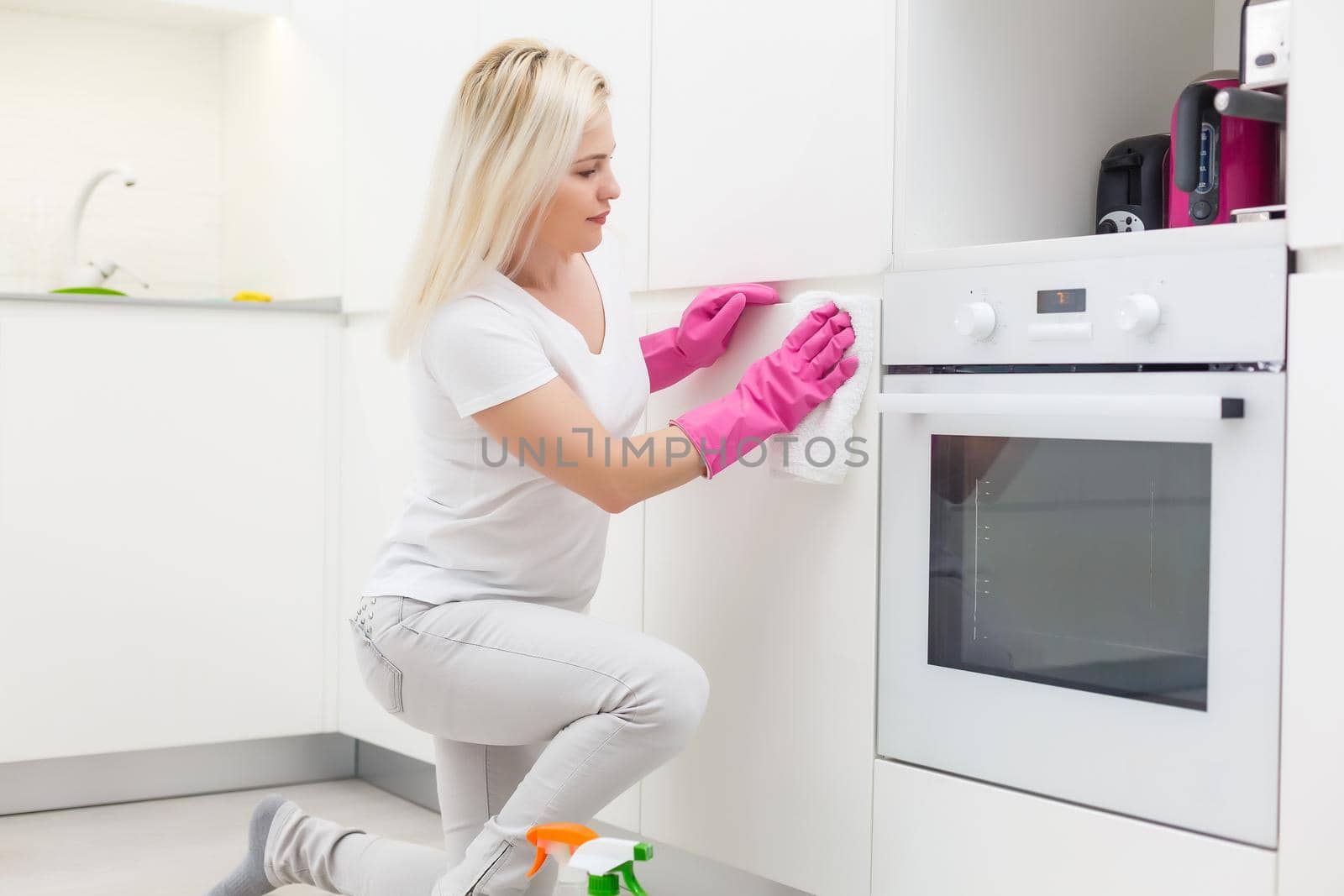 Woman in the kitchen is smiling and wiping dust using a spray and a duster while cleaning her house, close-up