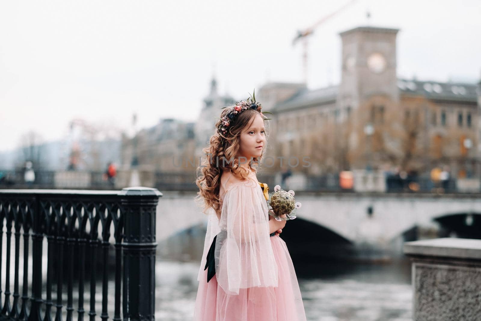 a little girl in a pink Princess dress with a bouquet in her hands walks through the old city of Zurich.Portrait of a girl in a pink dress on a city street in Switzerland.