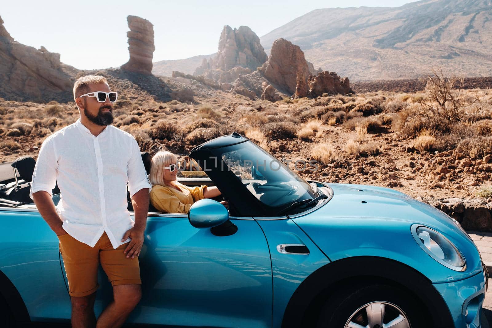 a woman and a man wearing glasses in a convertible car on a trip to the island of Tenerife. The crater of the Teide volcano, Canary Islands,Spain by Lobachad